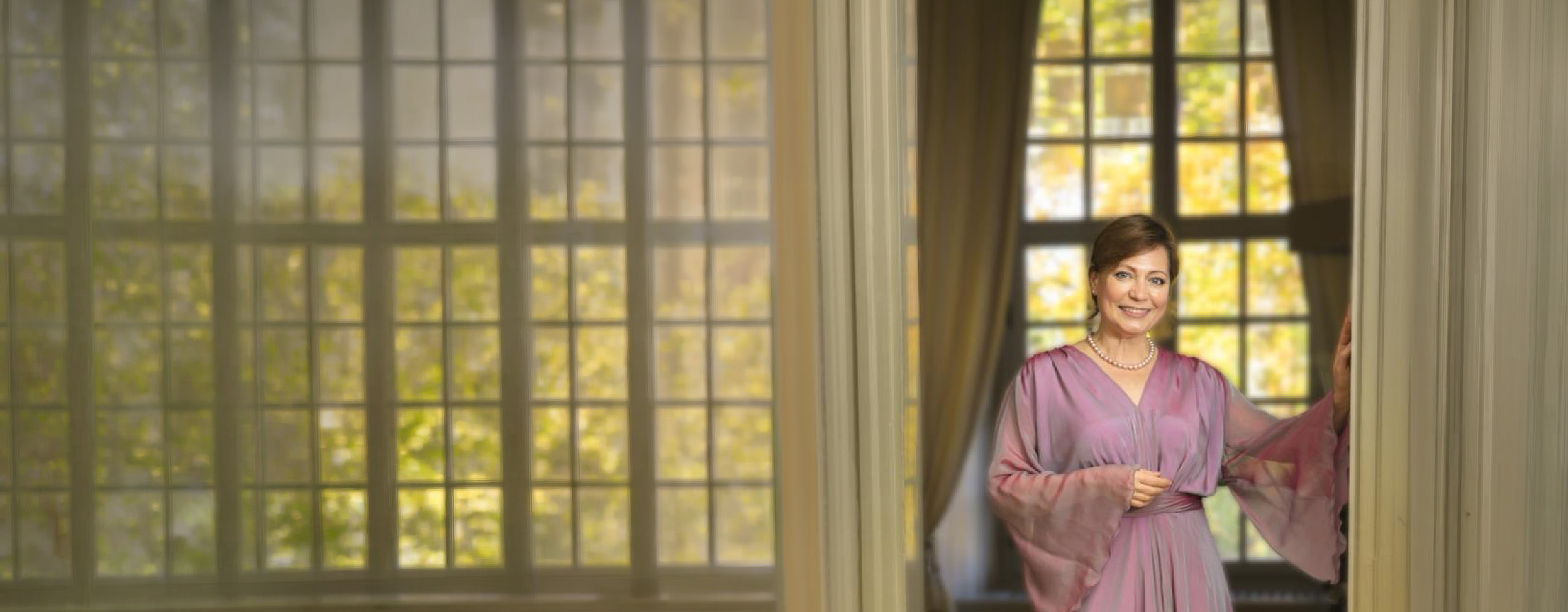 Olga Valmond im rosa Kleid in einem Türrahmen vor hohen Fenstern